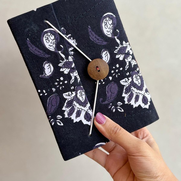 A hand block printed notebook in navy with a white paisley print and a button closure.