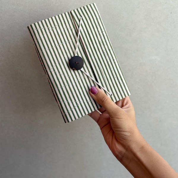A striped hand block printed notebook in olive and white, held in one hand.